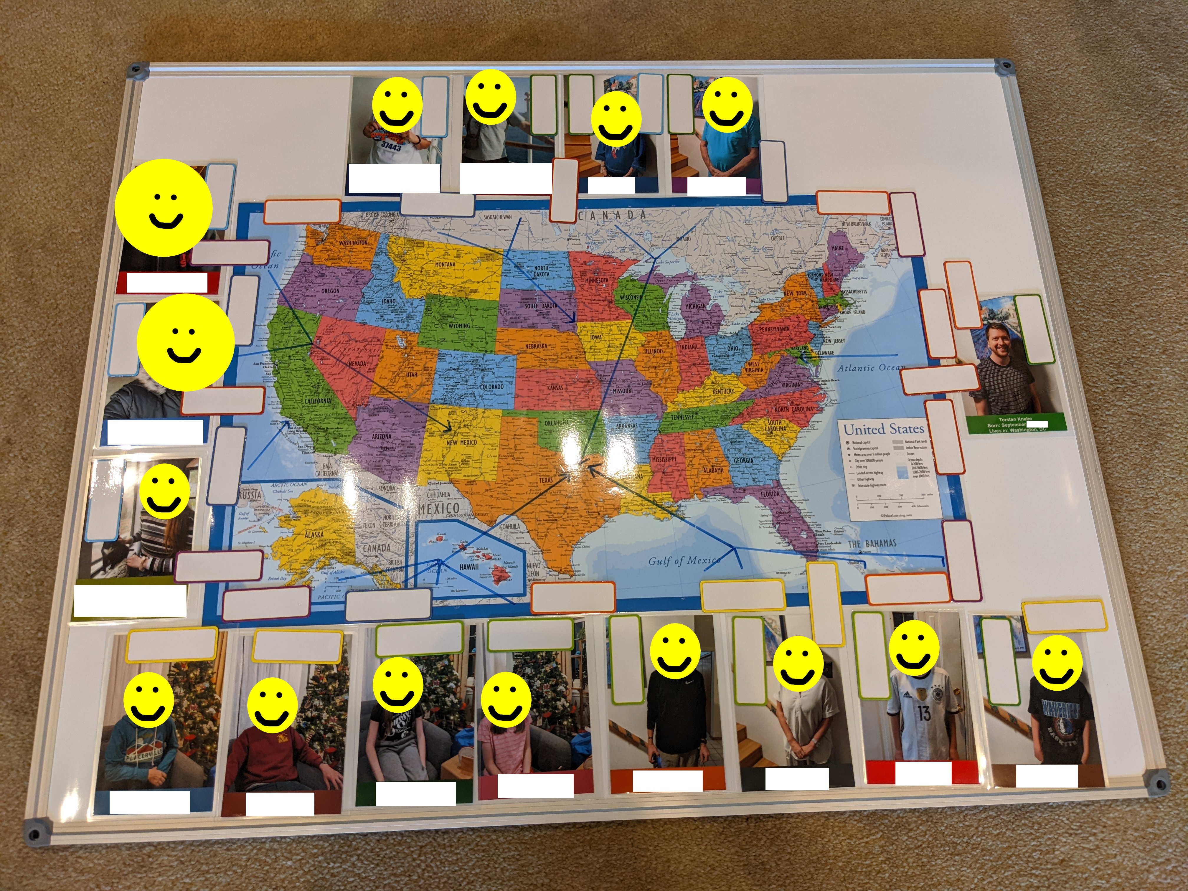 Whiteboard with a laminated US map in the center surrounded by 16 portraits of family members